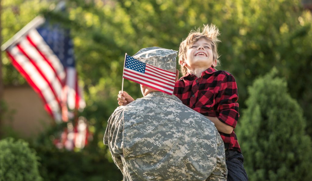 Child holding an American flag being held up by a soldier.